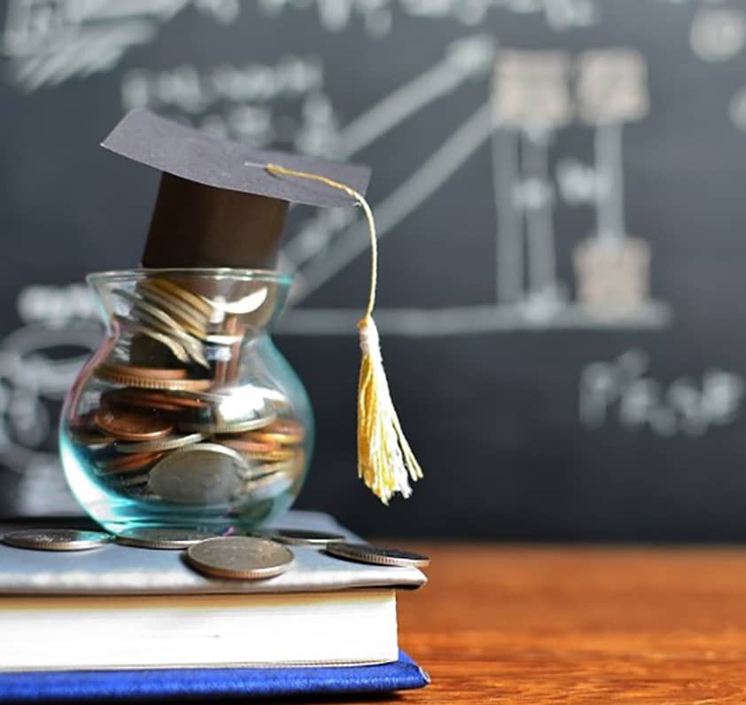 Glass jar filled with coins and a graduation cap on top.